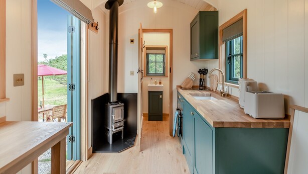 A compact kitchen with a wood-burning stove, a sink, and a window. - Set among the fruit trees with views of the fields. (Ongar)