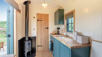 A compact kitchen with a wood stove, teal cabinets, and a window overlooking greenery.