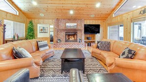 A cozy living room with leather sofas, a central fireplace, and wooden walls.