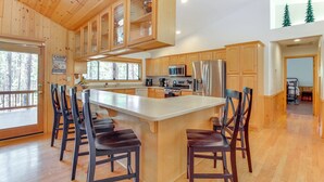 A cabin-style kitchen with wooden cabinets, a central island with bar stools, a refrigerator, and a microwave.