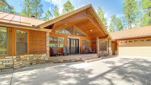 A log cabin with a stone foundation, a large front porch with Adirondack chairs, and a garage.