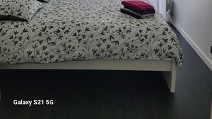 Un dormitorio con cama, un radiador, una ventana con cortinas y un cuadro en la pared.