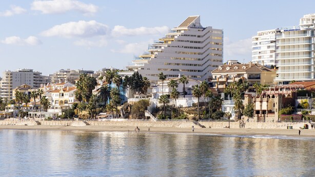 Un paisaje urbano costero con edificios modernos, palmeras y una playa.