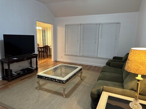 Una sala de estar con una televisión de pantalla plana, una mesa de centro de vidrio, un sofá verde y una lámpara.