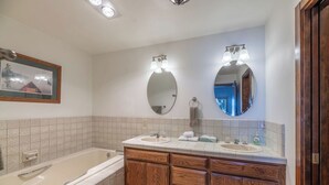 A bathroom with a bathtub, two sinks, wooden cabinets, and two wall-mounted mirrors with light fixtures. - Lakefront - 3 Bedroom (Hope)