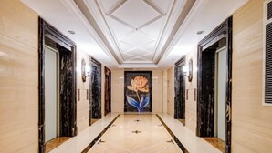 Un pasillo con suelo de mármol, una obra de arte floral en el centro y puertas con marcos negros.