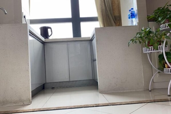 A corner of a room with a window, a potted plant, and a water bottle on the windowsill. - Kaiweina Hotel (Shengtai Road Subway Station Store) (Nanjing)