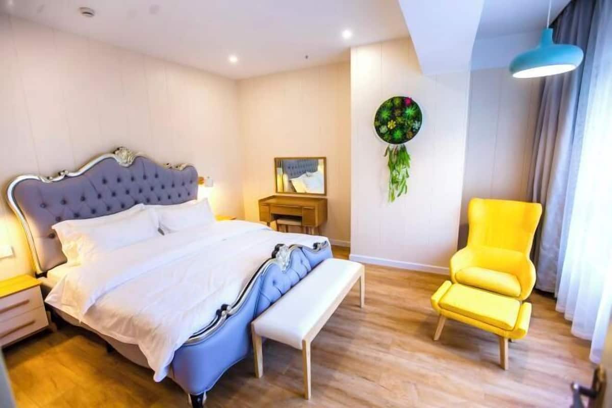 Ein Schlafzimmer mit Bett, Nachttisch, Bank, Stuhl und Wandbild.