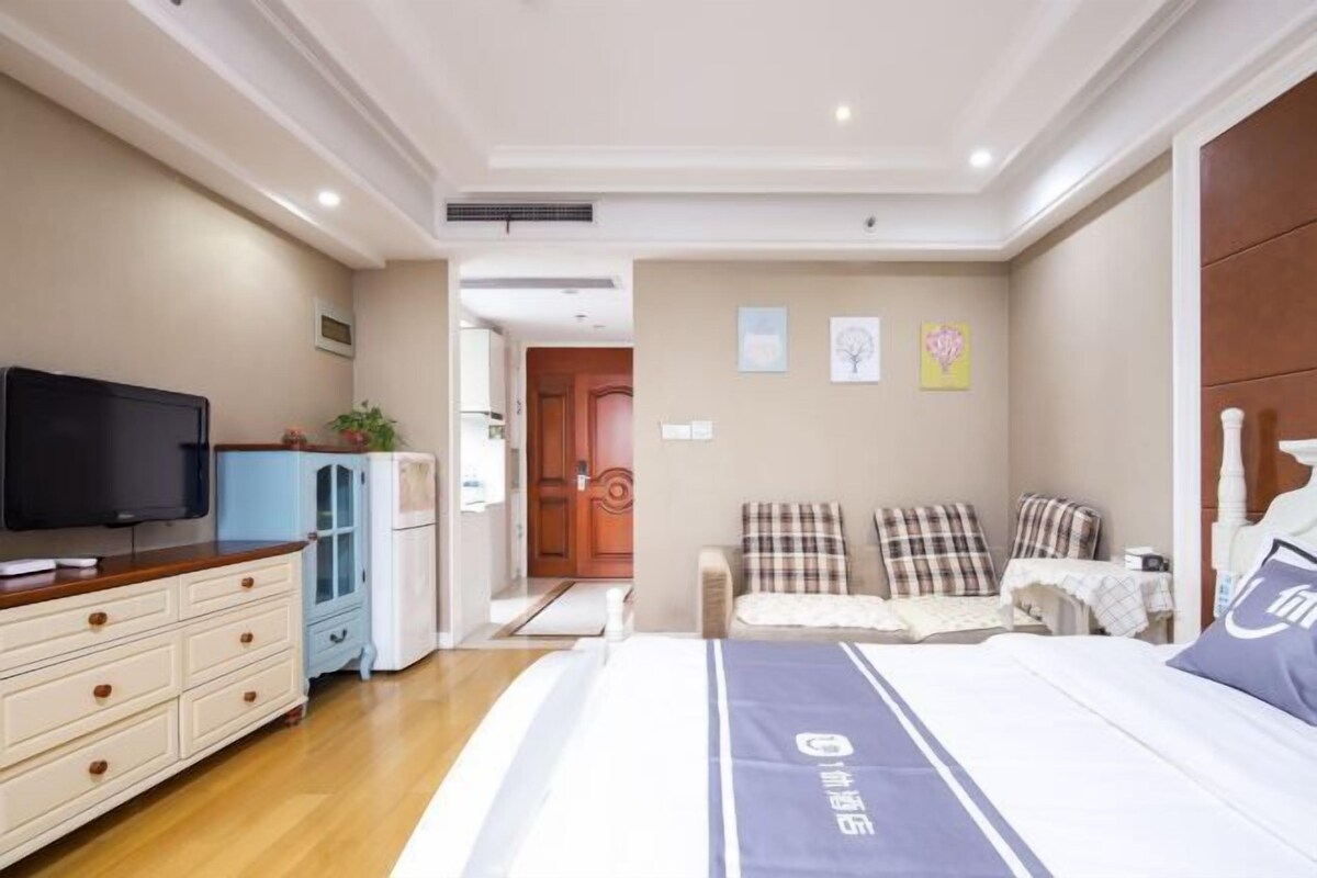 A bedroom with a bed, a television, a dresser, and a door leading to another room.