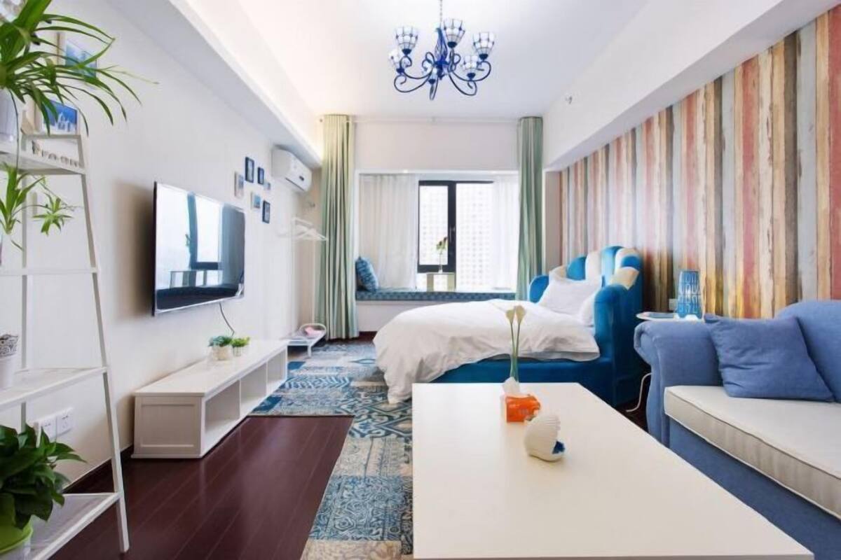 Ein modernes Hotelzimmer mit Bett, einer Couch, einem Fernseher, einer Kristallleuchtre und einer farbenfrohen Wand.