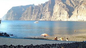A coastal beach with rocky cliffs, a boat in the water, and people enjoying the shore.