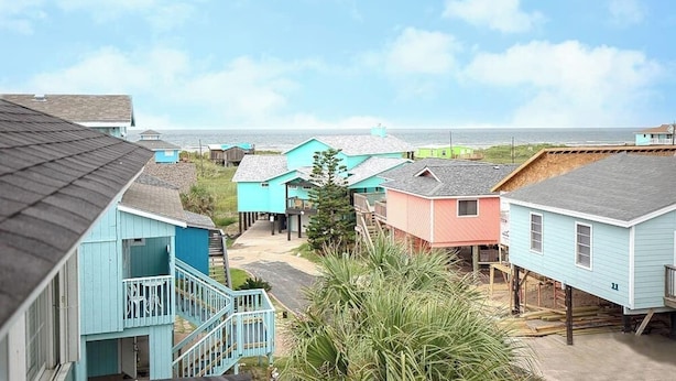 Een woongebied aan de kust met kleurrijke huizen, een trap die naar een veranda leidt, en uitzicht op de oceaan.