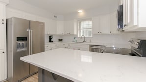 Een moderne keuken met witte kasten, een roestvrijstalen koelkast, een inbouwoven en een groot aanrecht.