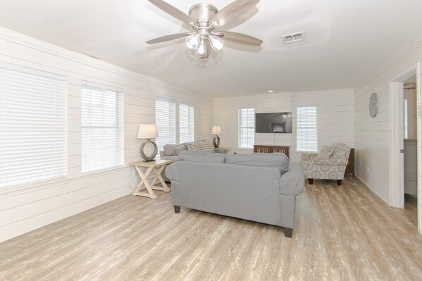 A spacious living room with a ceiling fan, a gray sofa, a patterned armchair, and a TV mounted on the wall.