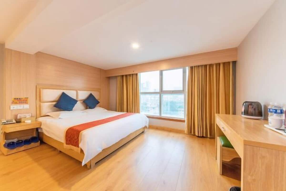 Habitación de hotel con cama, escritorio, ventana con cortinas y vistas a la ciudad.