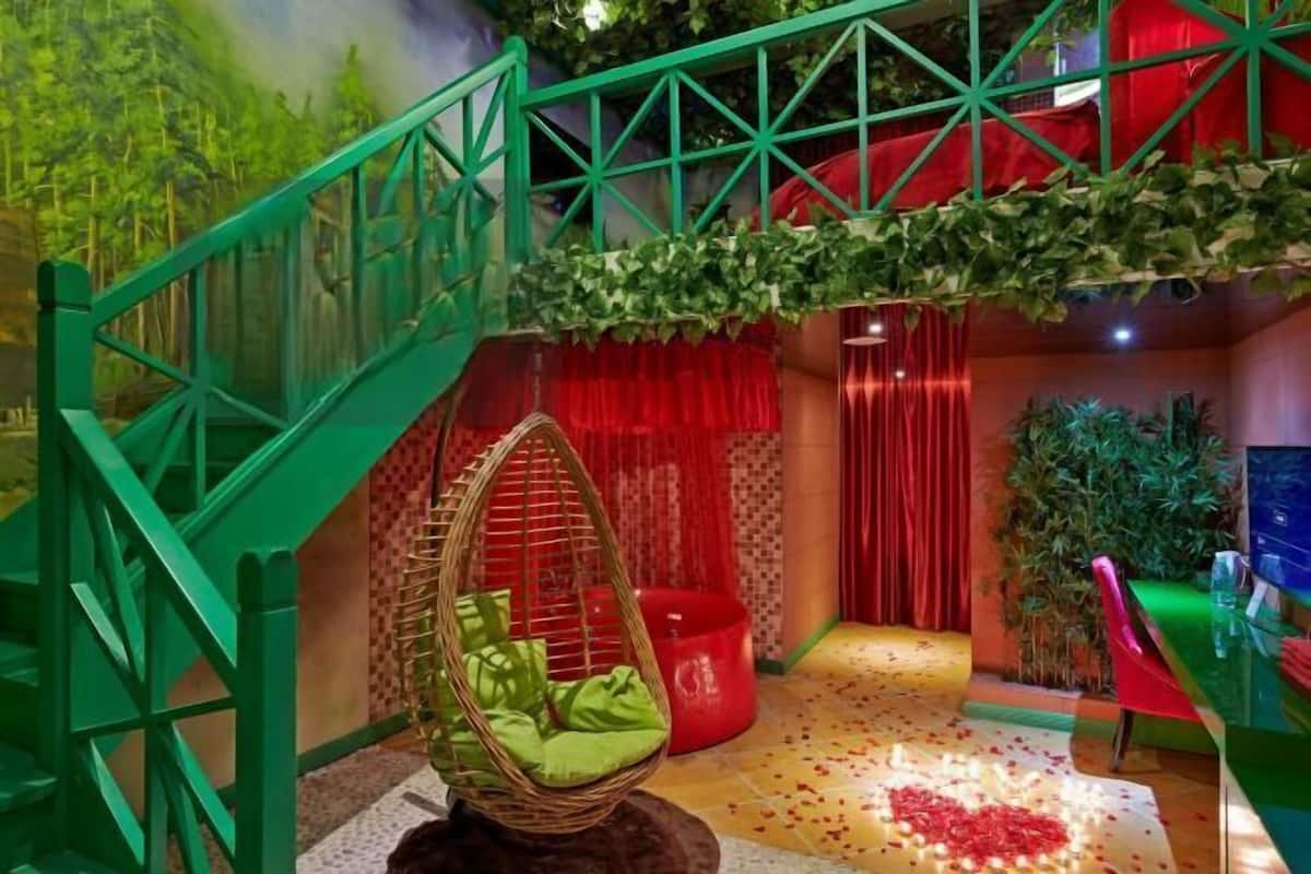 Una escalera con barandillas verdes, una silla colgante con cojines verdes, cortinas rojas y un cubo rojo.