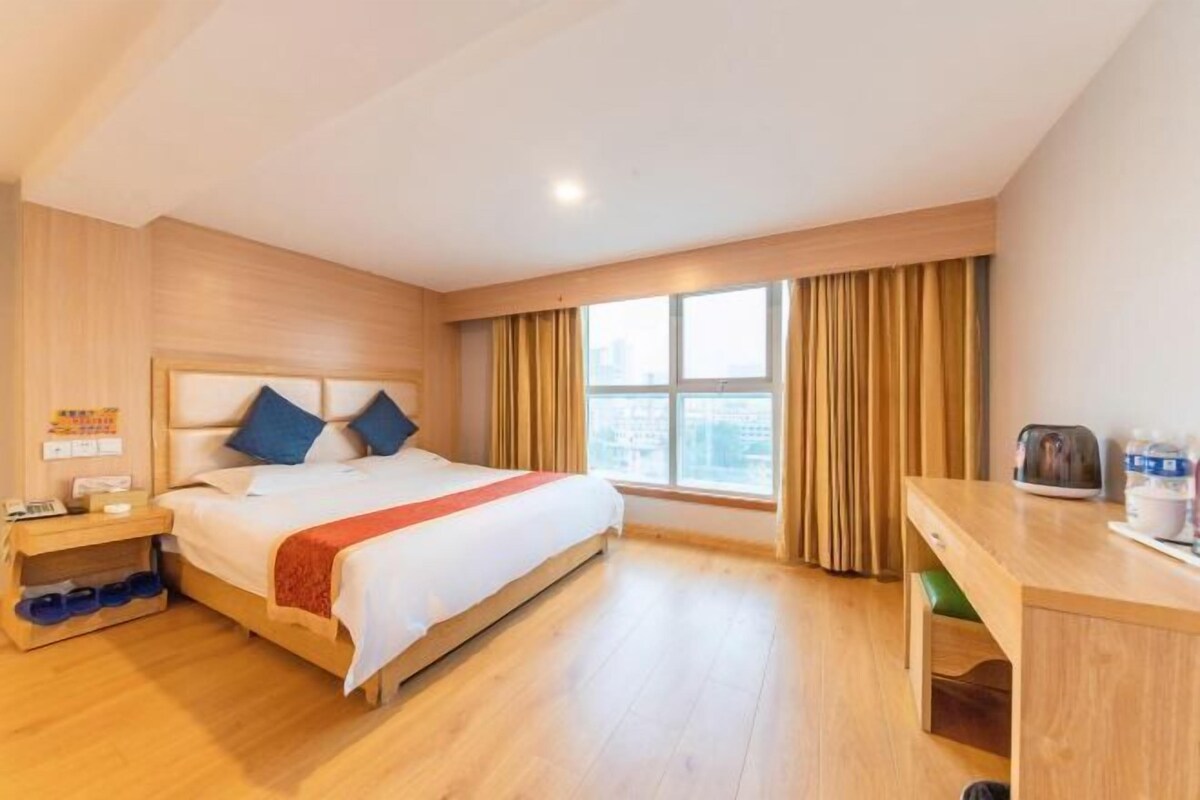 Habitación de hotel con cama, escritorio, ventana con cortinas y vista a la ciudad.