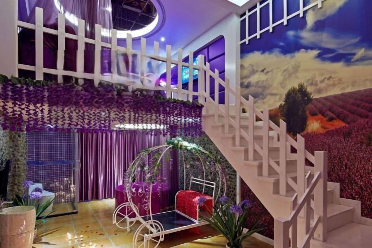 Una habitación con una escalera blanca, una cama con una colcha roja, una silla colgante y un mural de un paisaje.