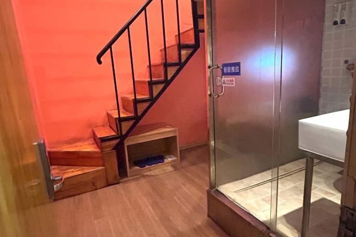 Un baño con cabina de ducha de vidrio, una escalera de madera y un lavamanos.