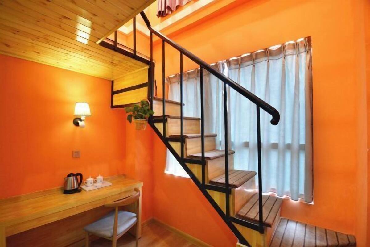 Una habitación con paredes naranja, un escritorio de madera con hervidor, una lámpara y una escalera con barandillas negras.