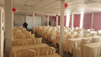 Un salón de banquetes con filas de mesas, sillas y decoraciones rojas.