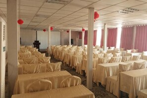 A banquet hall with rows of tables, chairs, and red decorations. - Haixin Youth Hotel (Zhengzhou)