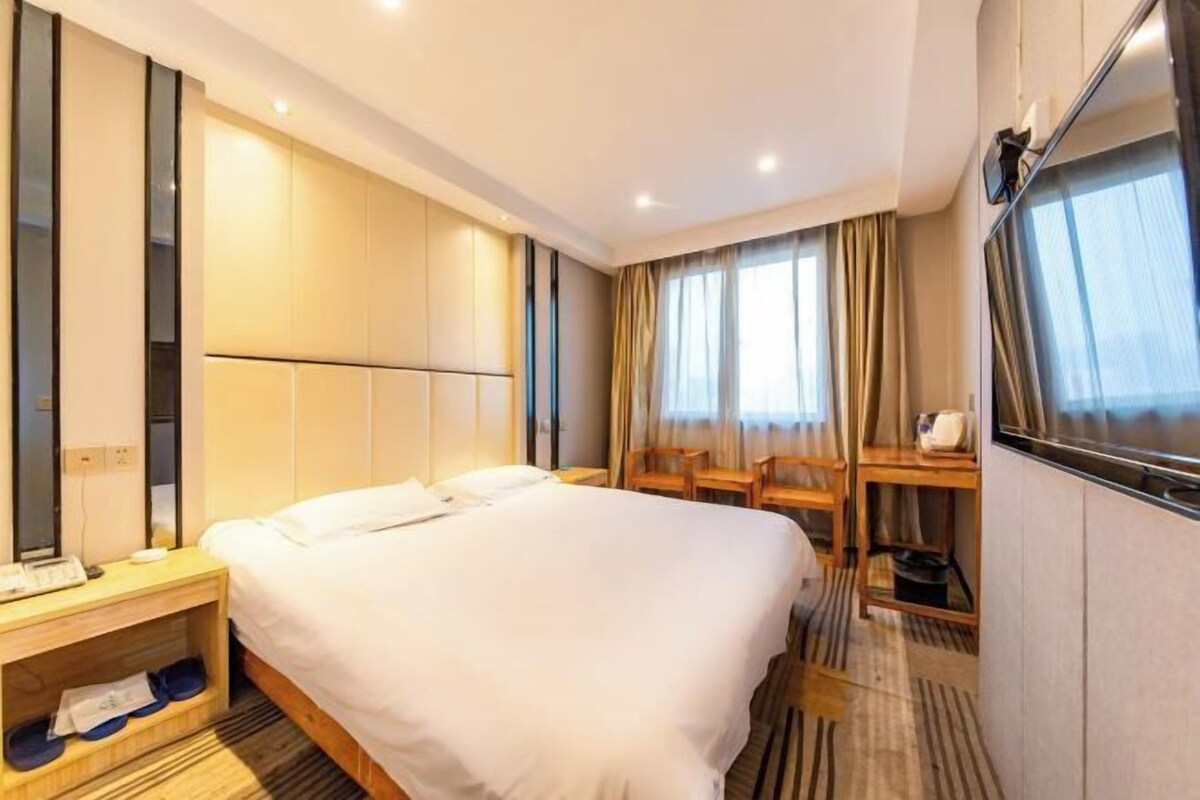 Habitación de hotel con una cama grande, un escritorio, una silla, un espejo y una ventana con cortinas.