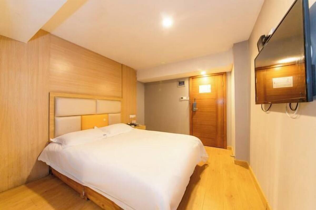 Una habitación de hotel con cama, paneles de madera, televisor y una puerta.