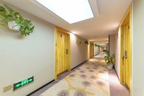Un pasillo de hotel con alfombra estampada, puertas de madera y plantas en macetas.