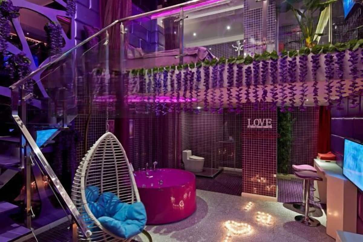 Un baño moderno con una decoración morada, una silla colgante y una bañera rosa.