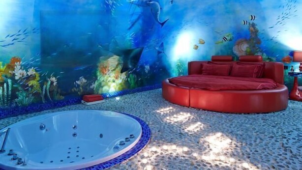 Een kamer met een grote aquariumwand, een ronde rode bank en een jacuzzi.