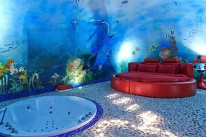 Una stanza con una parete grande di acquario, un divano rosso arrotondato e una vasca idromassaggio.