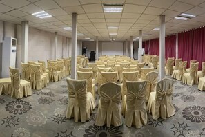 Une salle de conférence avec des rangées de chaises, une scène et un rideau rouge en arrière-plan.