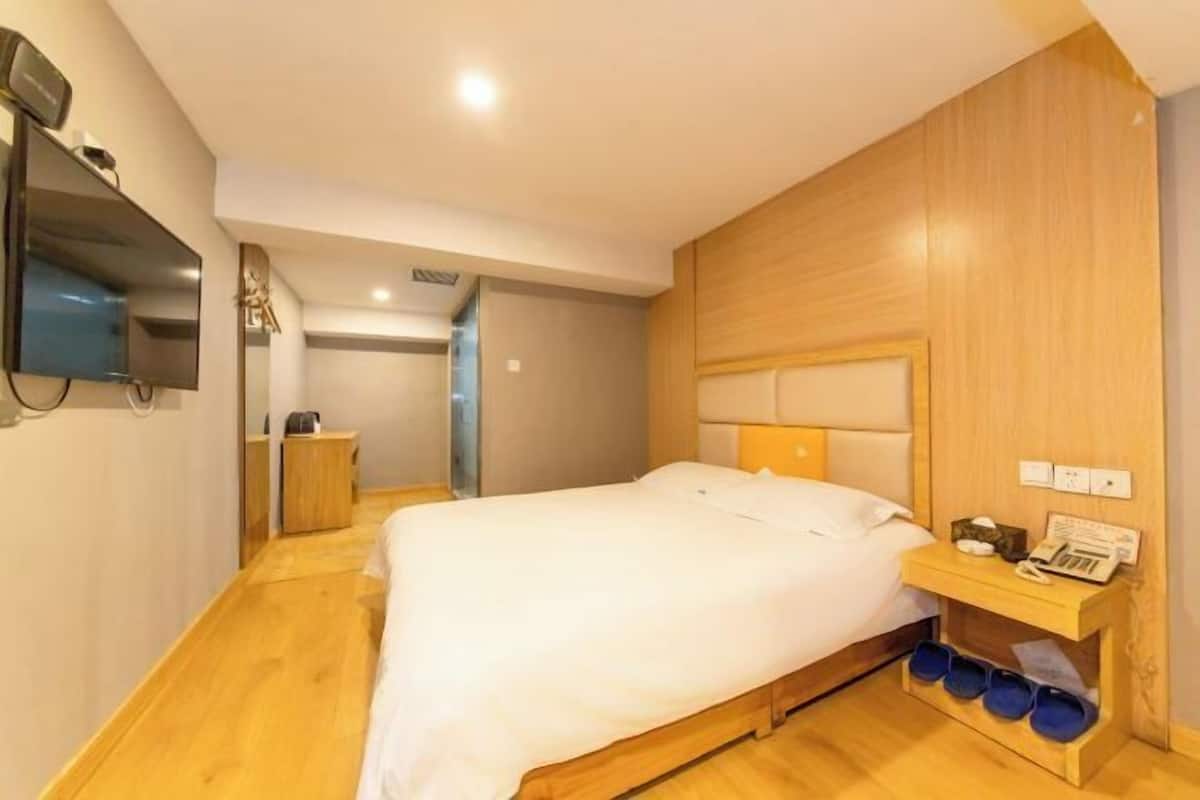 Un dormitorio con cama, cabecero de madera, mesita de noche con teléfono y libros, y televisor montado en la pared.