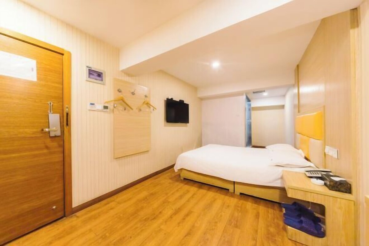 Una habitación de hotel con piso de madera, una cama individual, una mesita de noche con lámpara, un armario y un televisor pequeño.