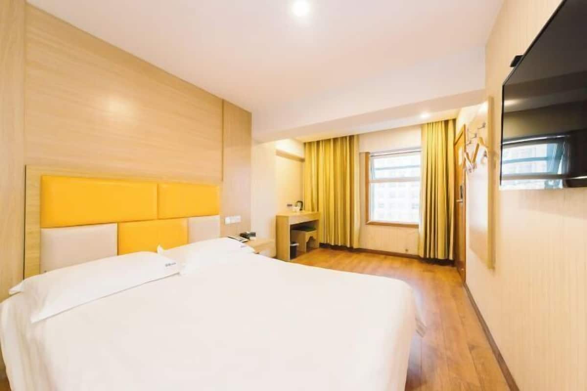 Habitación de hotel con una cama grande, un escritorio, una silla, un televisor y una ventana con cortinas.