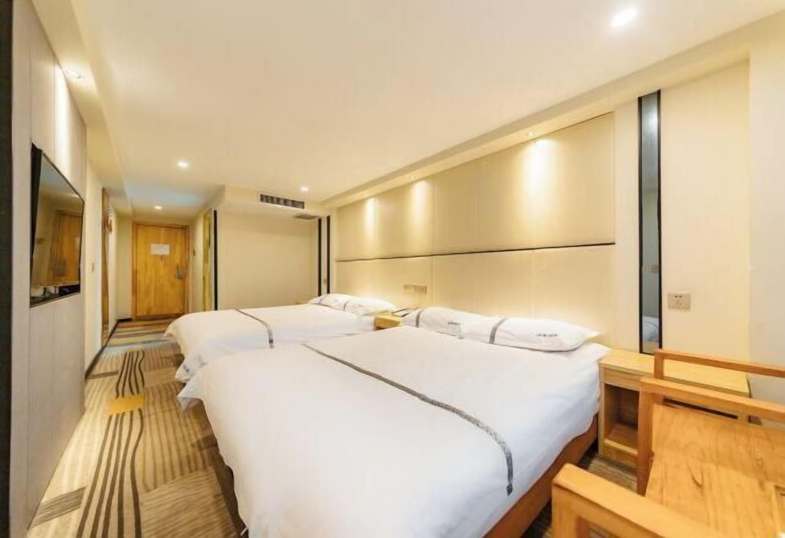 A hotel room with two beds, a wooden bench, a mirror, and a patterned carpet.