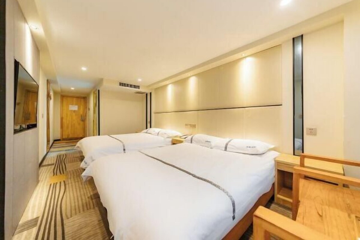 Una habitación de hotel con dos camas, un banco de madera, un espejo y una alfombra estampada.