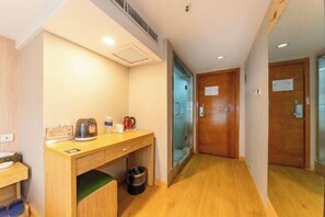 Una habitación de hotel con un escritorio de madera, una tetera y un cubo de basura.