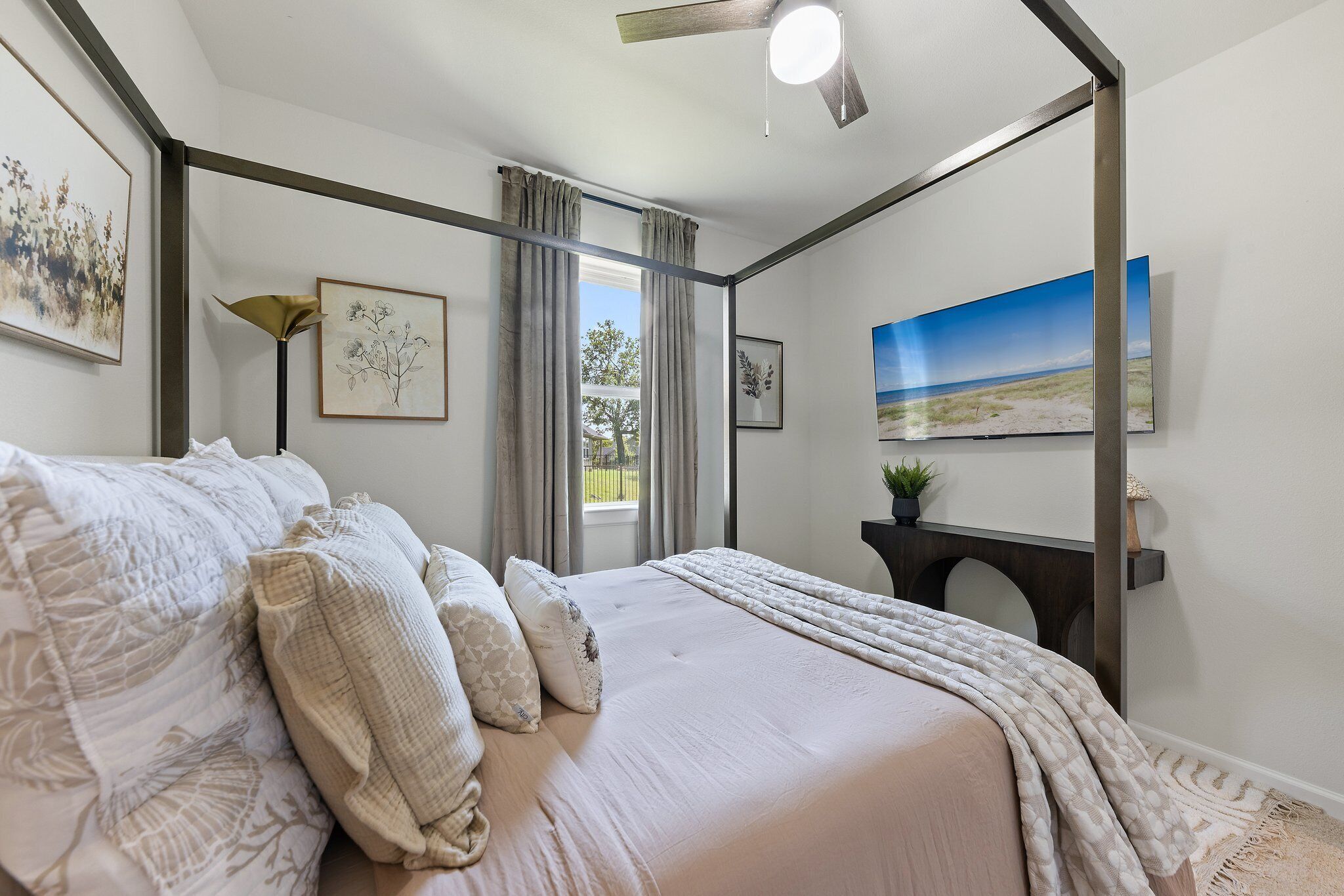 Een slaapkamer met een bed, een plafondventilator, een raam met gordijnen en wanddecoratie.