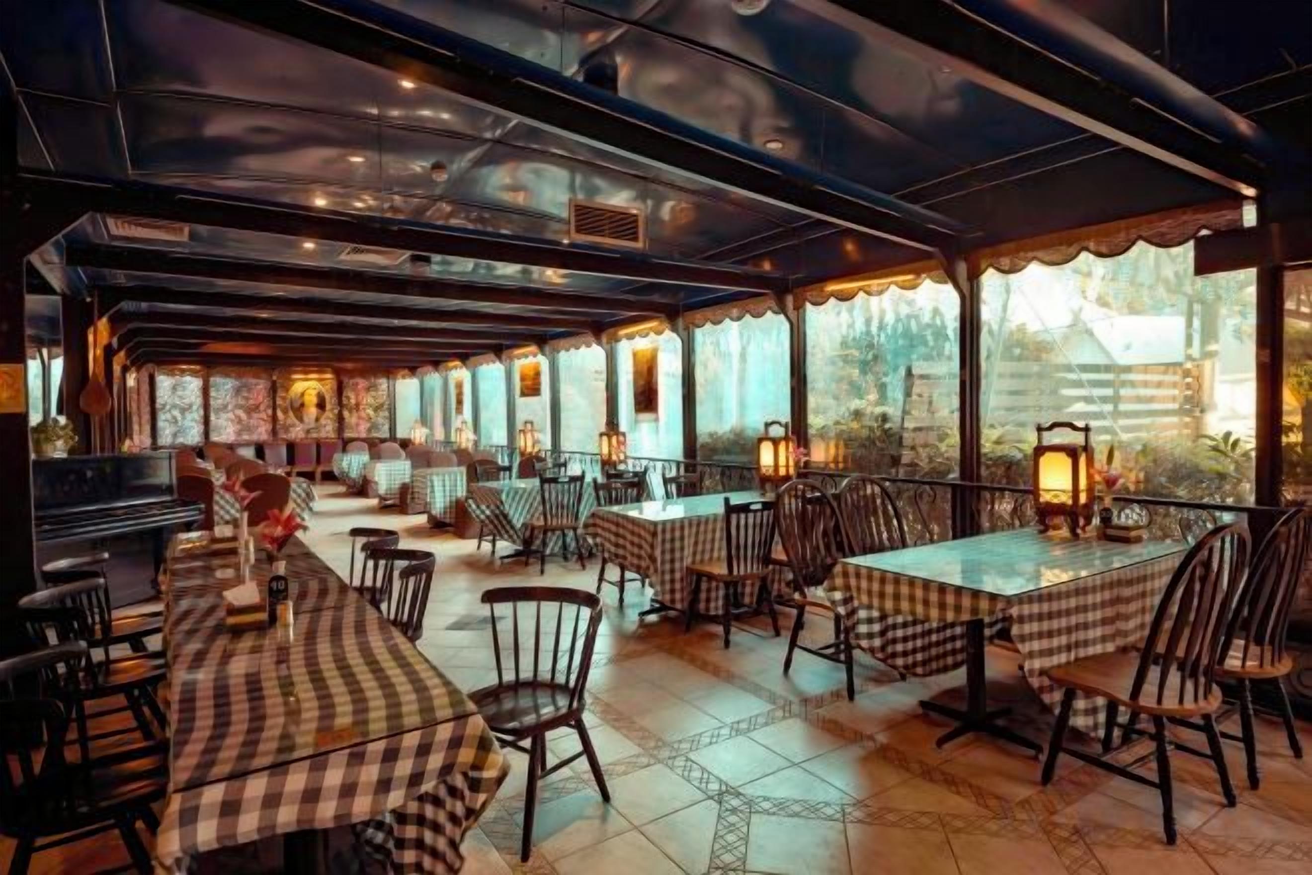 An outdoor restaurant with tables and chairs, covered by a roof, and large windows.