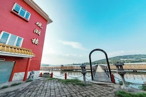 A red building with a visible entrance and a pathway leading to a bridge over water.