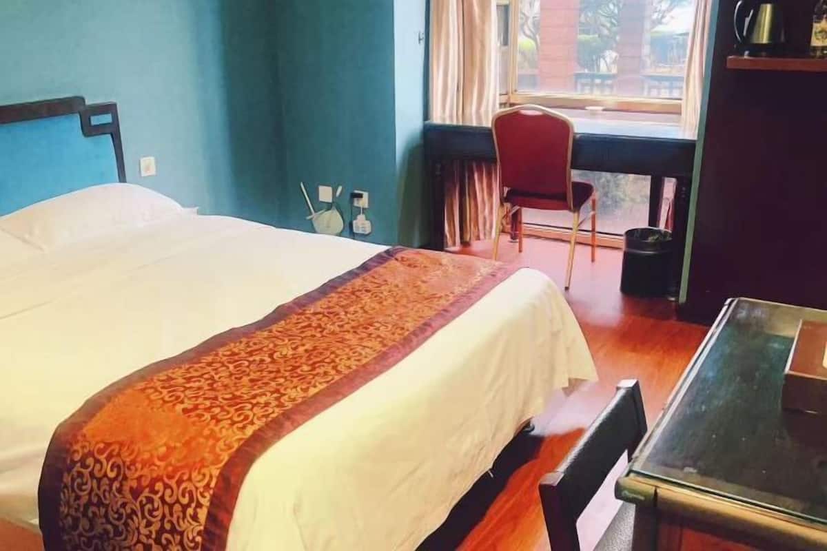 A hotel room with a bed, a desk, a chair, and a window.