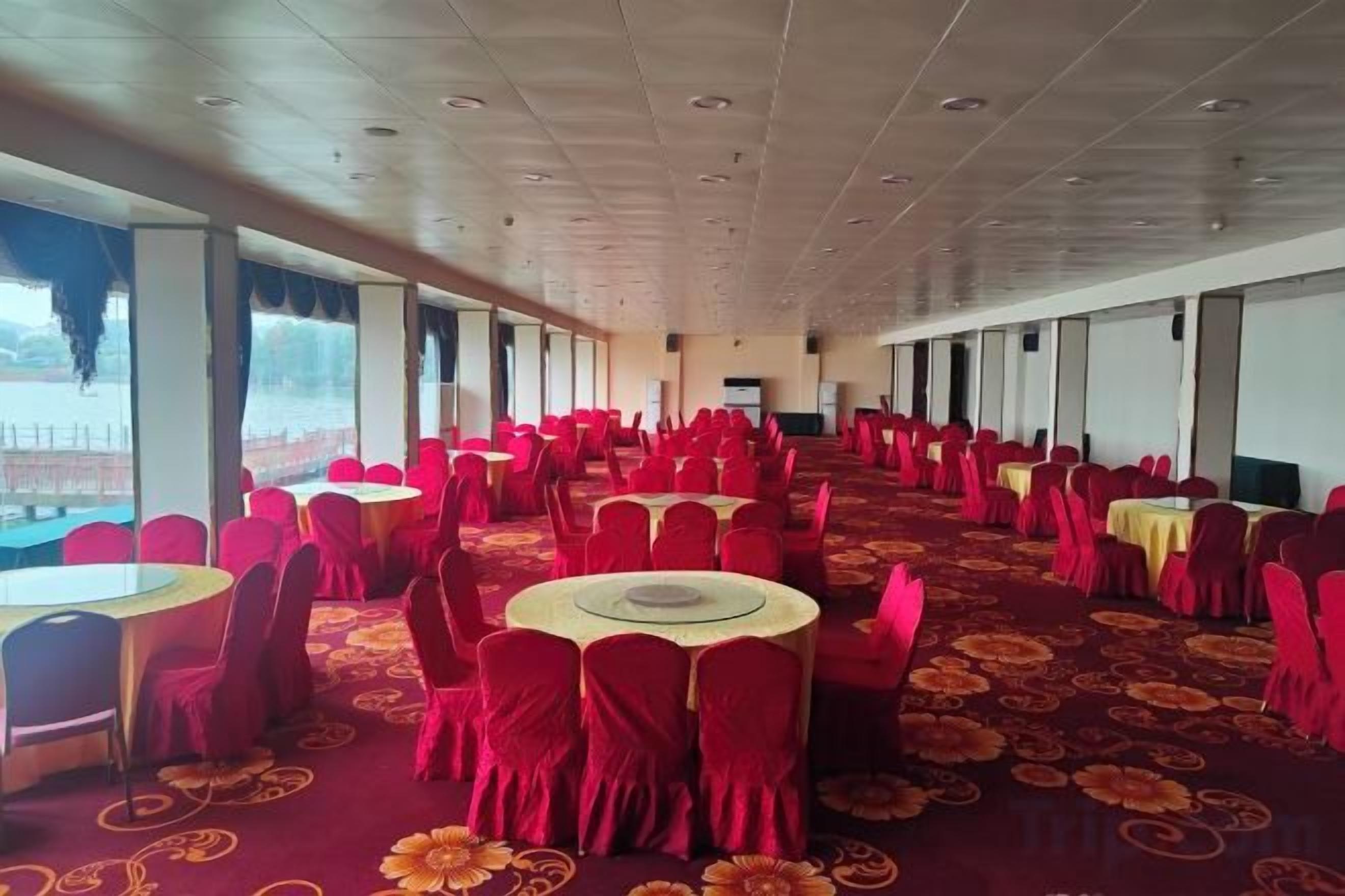 A banquet hall with round tables and chairs, large windows, and a carpeted floor.