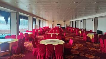 A banquet hall with round tables and chairs, large windows, and a carpeted floor.
