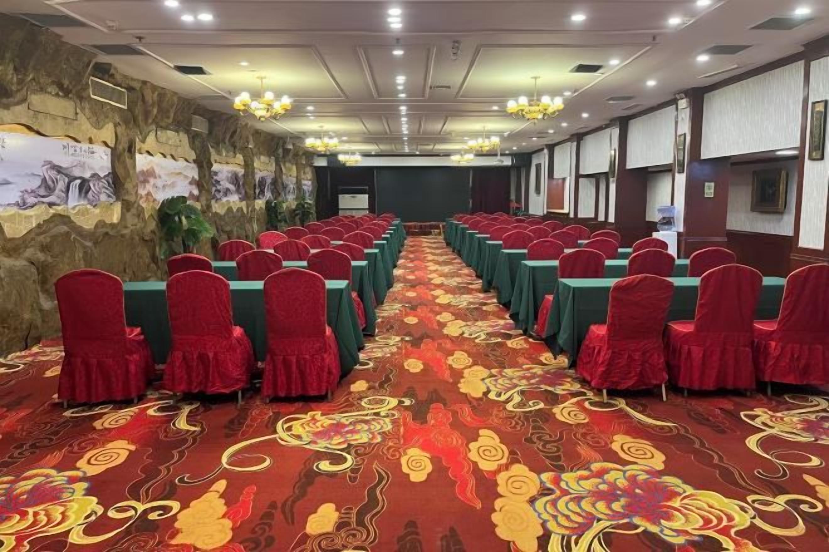 Une salle de conférence avec des rangées de tables et de chaises, une moquette à motifs et une fresque murale.