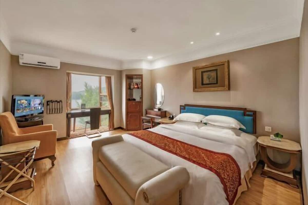 A hotel room with a large bed, a television, a desk, and a balcony with a view.