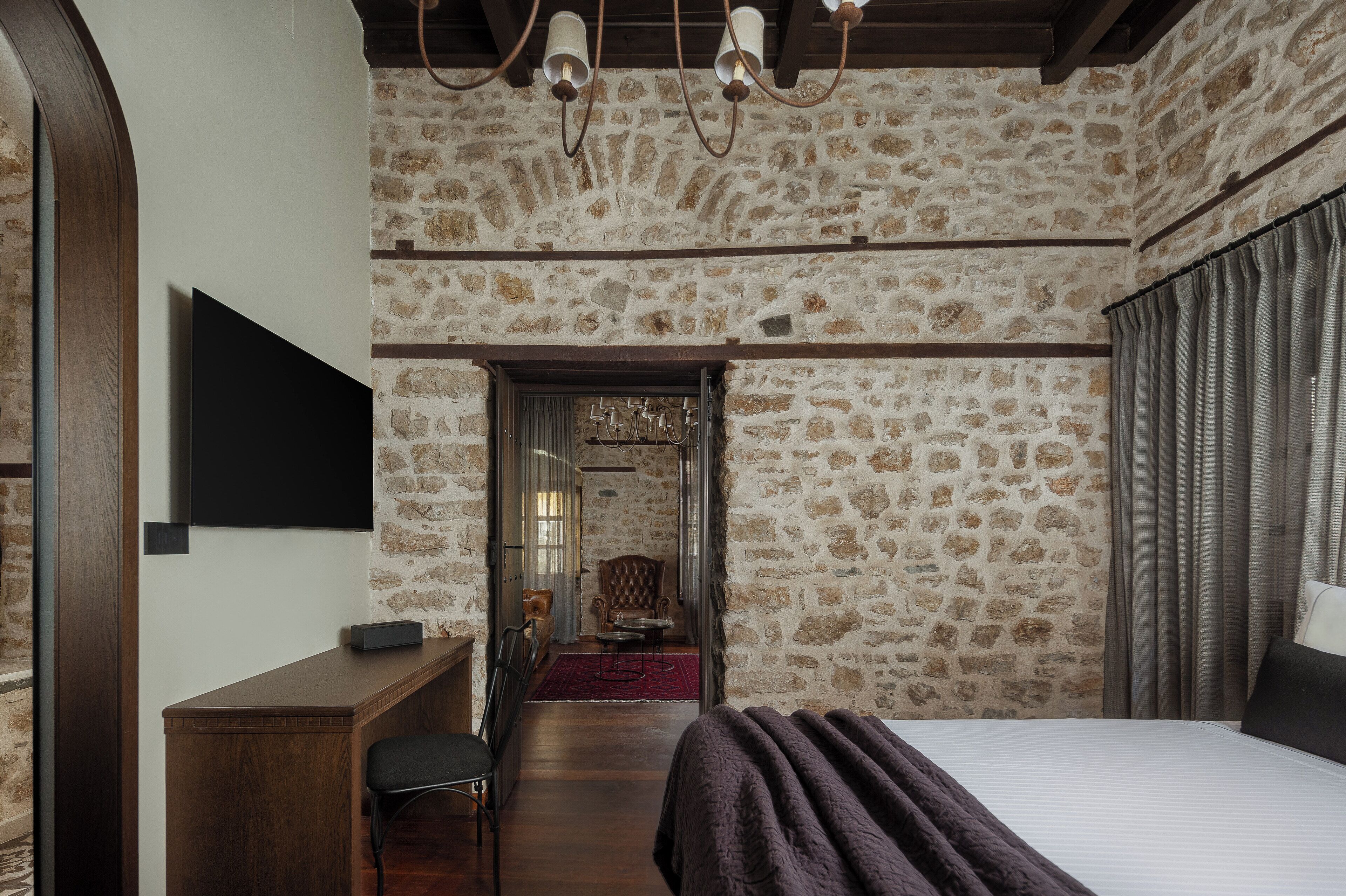 A bedroom with a stone wall, a bed, a desk, and a TV.