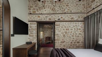 A bedroom with a stone wall, a bed, a desk, and a TV.