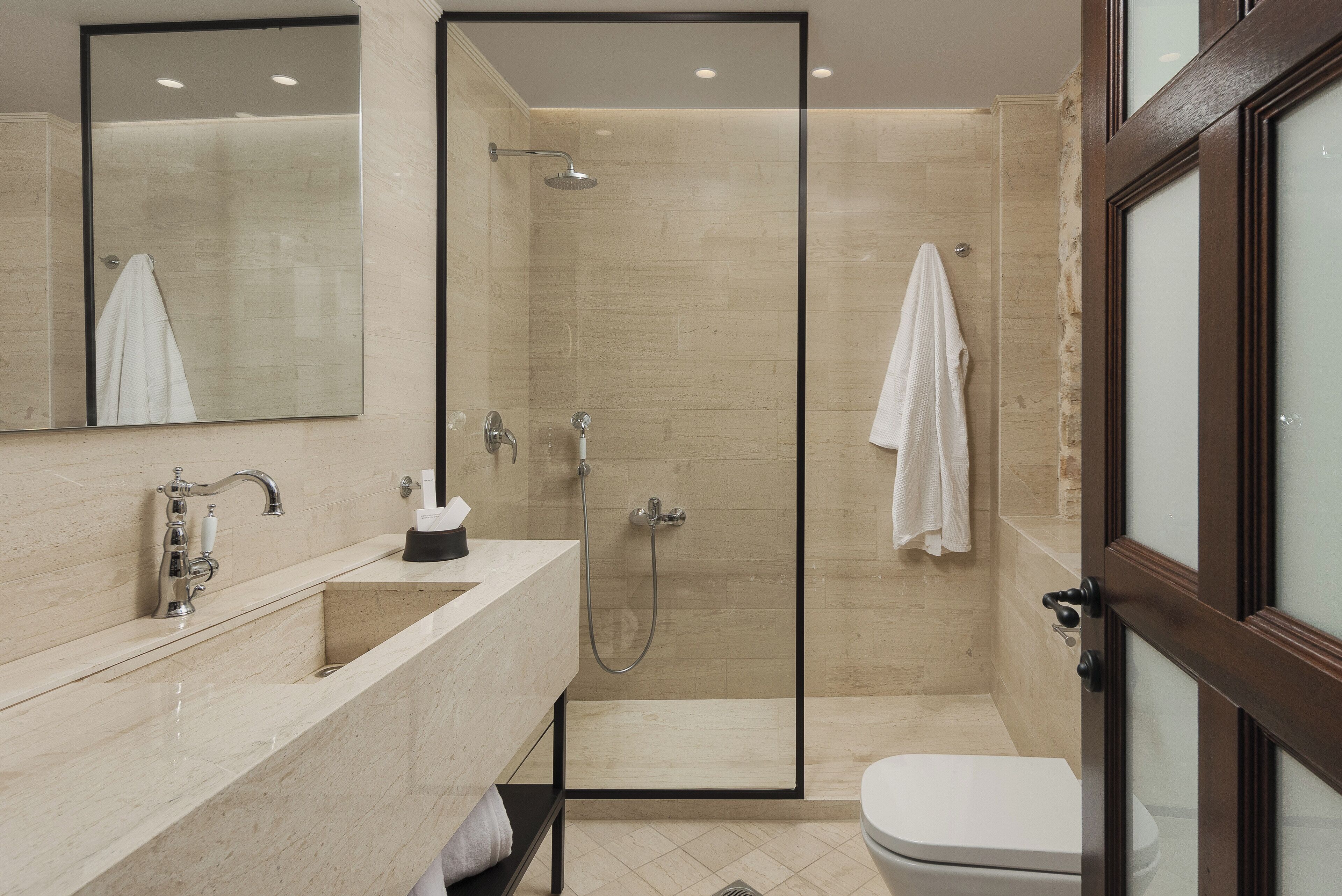 A modern bathroom with a glass-enclosed shower, a marble sink, and a white toilet.